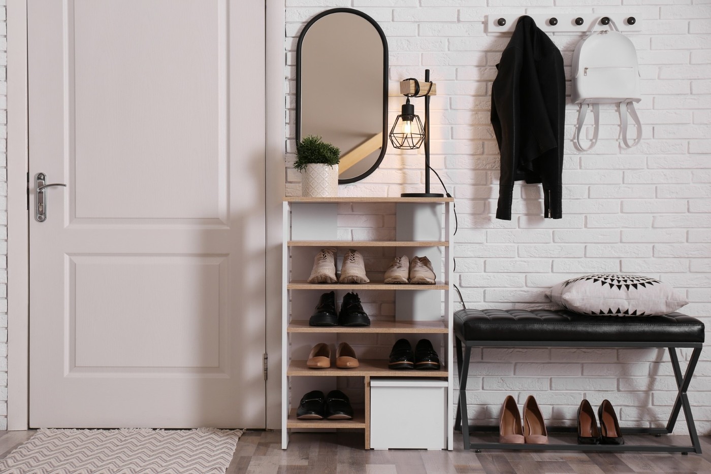 Shelving unit with shoes and different accessories near white brick wall in hall. Storage idea
